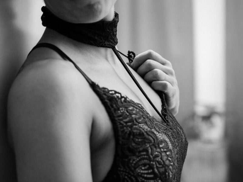 Sort-hvid detalje af kvinde i blondebody med halschoker, hånd justerer skulderstrop