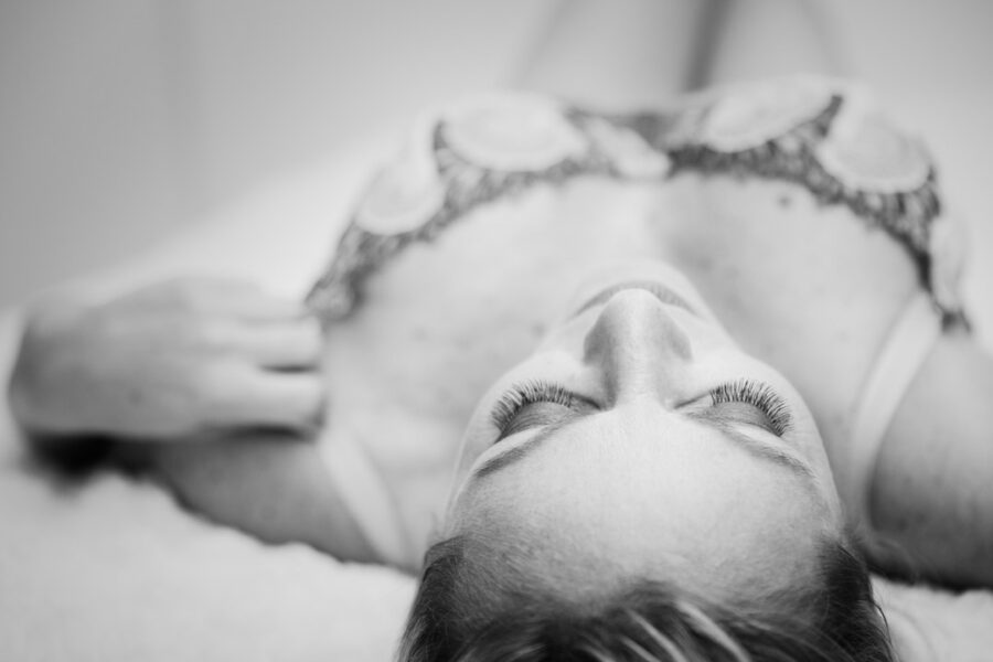 Sort-hvid overhead af kvinde i broderet bh, liggende med lukkede øjne og fremhævede øjenvipper