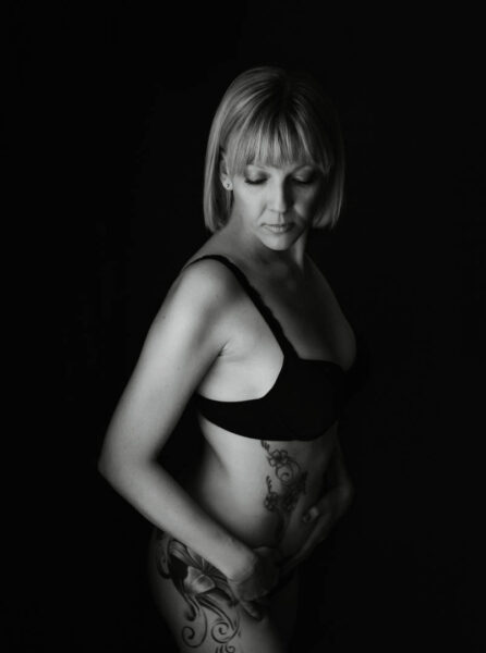 Low-key sort-hvid boudoirportræt af kvinde, der ser nedad i bh og med blomster-tatovering