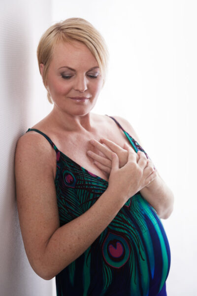 Højlys graviditetsfoto af kvinde i farverig kjole, der hviler hænderne over hjertet med lukkede øjne