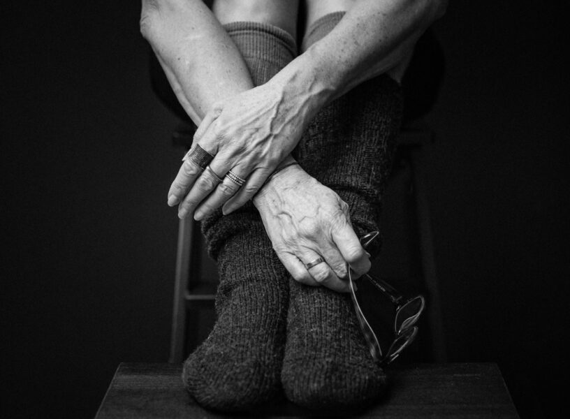 Intimt sort-hvid detaljebillede af ældre kvindehænder med smykker, strikstrømper og briller