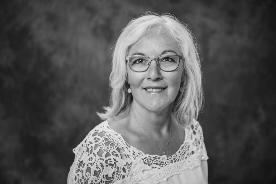 Sort-hvid studieportræt af moden kvinde med briller og kort hvidt hår, der smiler venligt