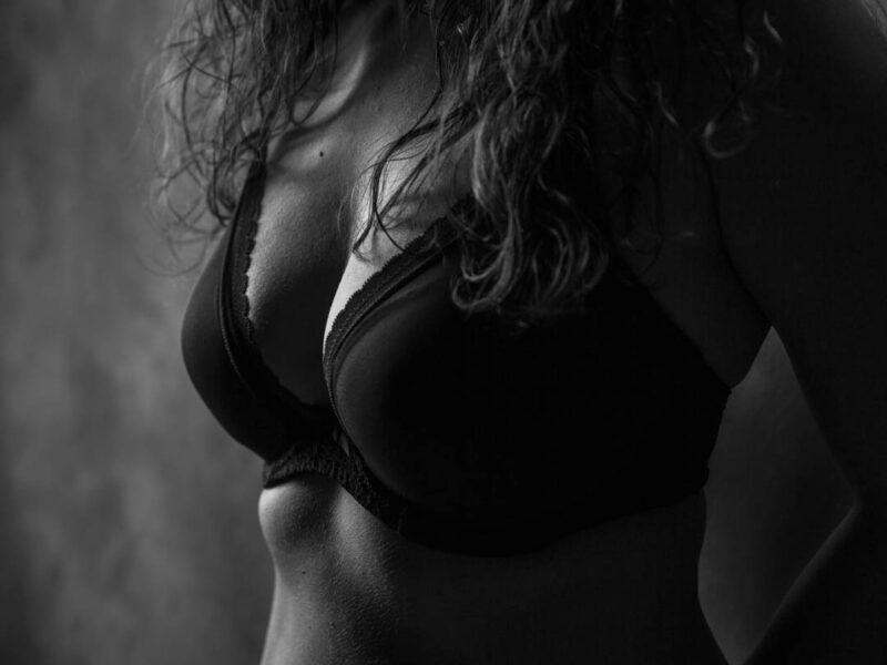 Low-key sort-hvid portræt af kvindetorso med våde krøller og sort bh, dramatisk sidebelysning