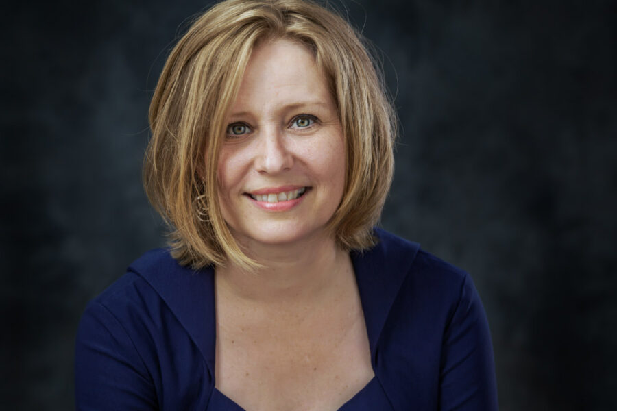 Professionelt headshot af smilende kvinde i marineblå kjole foran mørk, blød baggrund